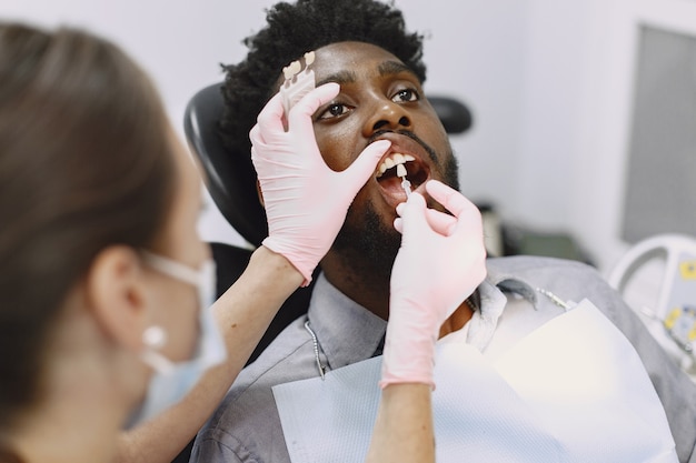 Photo gratuite jeune homme afro-américain. guy visitant le cabinet du dentiste pour la prévention de la cavité buccale. homme et médecin de famille pendant le contrôle des dents.