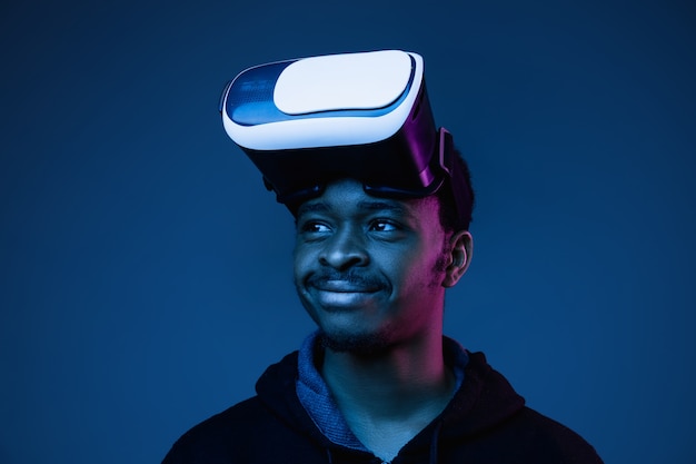Jeune homme afro-américain jouant dans des lunettes VR en néon sur gradient