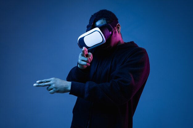 Jeune homme afro-américain en lunettes VR en néon sur fond bleu. Portrait masculin