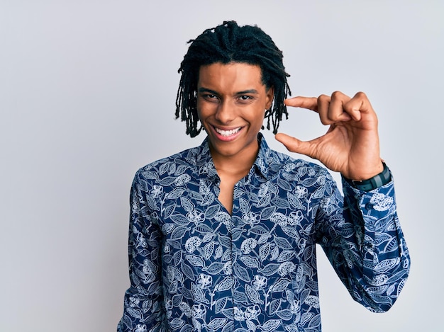 Photo gratuite jeune homme afro-américain portant une chemise de style années 80 souriant et confiant gesticulant avec la main faisant un signe de petite taille avec les doigts regardant et la caméra. notion de mesure.
