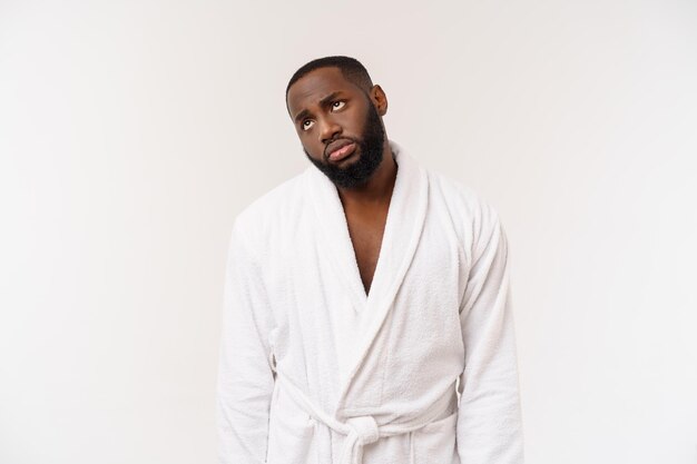 Jeune homme afro-américain portant un peignoir sur fond blanc isolé pensant avoir l'air fatigué et ennuyé par des problèmes de dépression