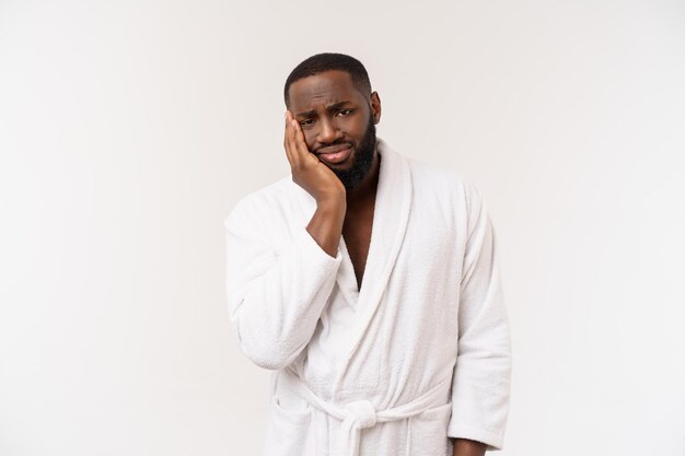 Jeune homme afro-américain portant un peignoir sur fond blanc isolé pensant avoir l'air fatigué et ennuyé par des problèmes de dépression