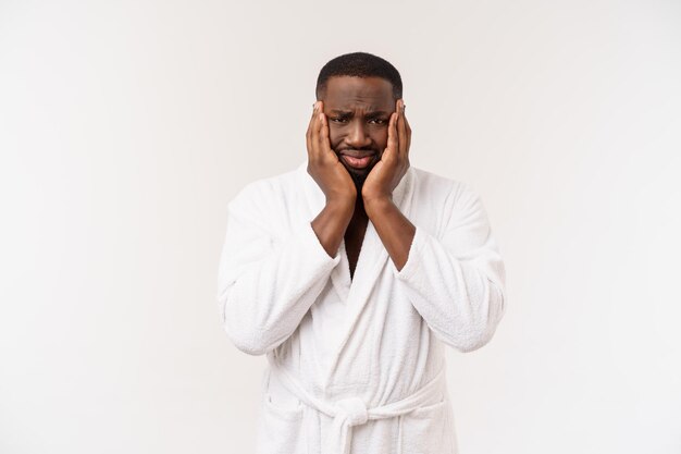 Jeune homme afro-américain portant un peignoir sur fond blanc isolé pensant avoir l'air fatigué et ennuyé par des problèmes de dépression