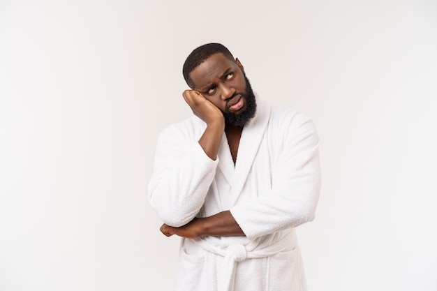 Jeune homme afro-américain portant un peignoir sur fond blanc isolé pensant avoir l'air fatigué et ennuyé par des problèmes de dépression