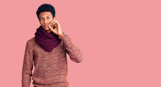 Photo gratuite jeune homme afro-américain portant un pull d'hiver décontracté et une écharpe bouche et lèvres fermées comme une fermeture éclair avec les doigts secret et tabou silencieux parlant
