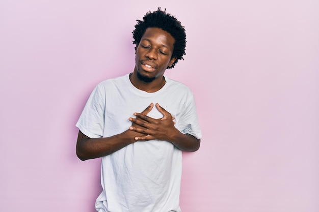 Photo gratuite jeune homme afro-américain portant un t-shirt blanc décontracté souriant avec les mains sur la poitrine avec les yeux fermés et un geste reconnaissant sur le concept de santé du visage