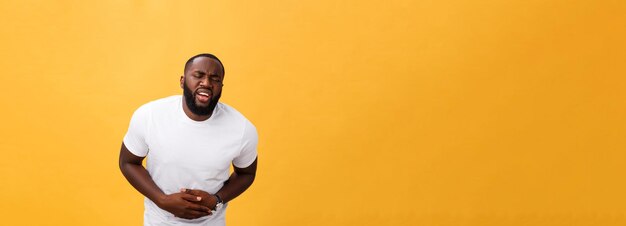 Jeune homme afro-américain portant un t-shirt blanc avec la main sur le ventre parce que la nausée est une maladie douloureuse