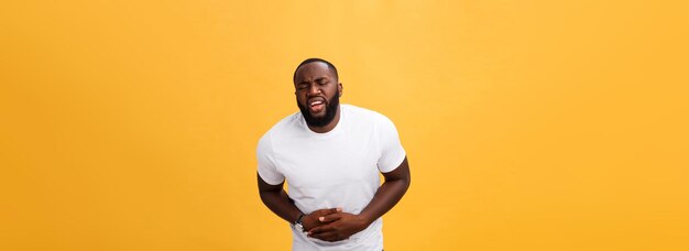 Jeune homme afro-américain portant un t-shirt blanc avec la main sur le ventre parce que la nausée est une maladie douloureuse