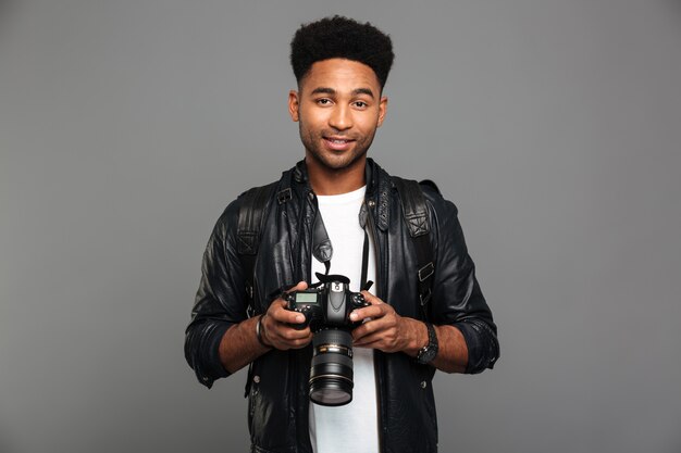 Jeune homme afro américain souriant attrayant tenant un appareil photo numérique, à la recherche