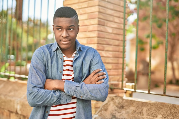 Jeune homme afro-américain souriant heureux avec le geste des bras croisés à la ville