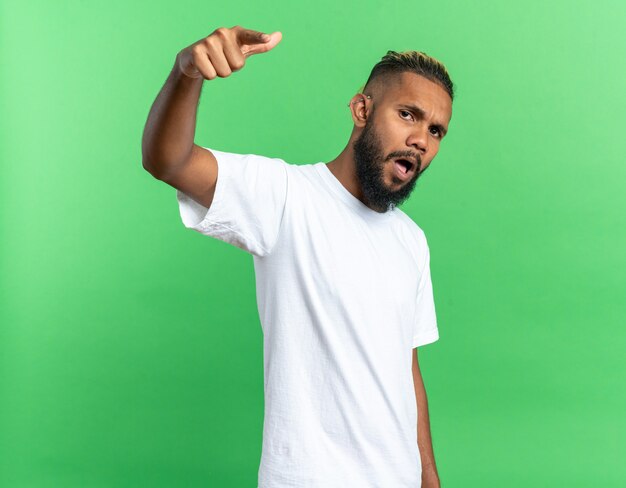 Jeune homme afro-américain en t-shirt blanc pointant avec l'index à la caméra en colère