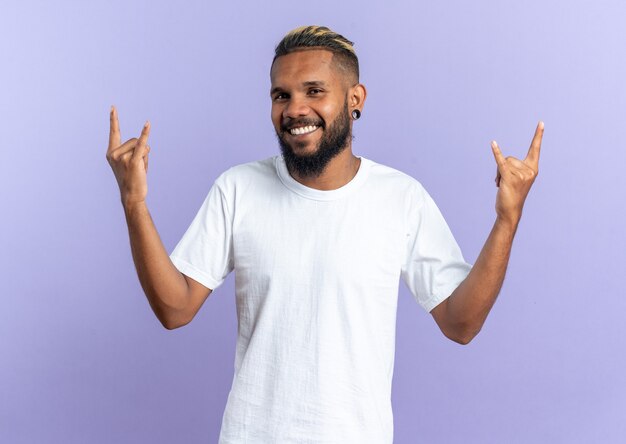 Jeune homme afro-américain en t-shirt blanc regardant la caméra souriant heureux et joyeux montrant le symbole du rock