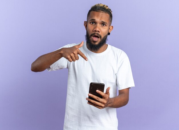 Jeune homme afro-américain en t-shirt blanc tenant un smartphone pointant