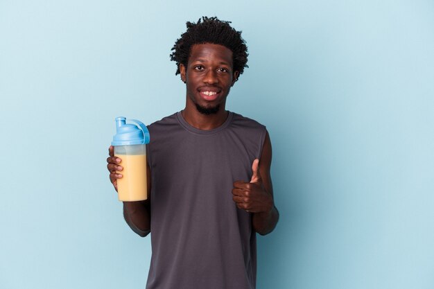 Jeune homme afro-américain tenant un milk-shake protéiné isolé sur fond bleu souriant et levant le pouce vers le haut