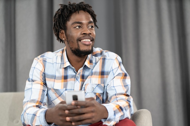 Jeune homme afro-américain tenant un smartphone à la main en détournant les yeux