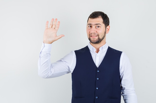 Jeune homme agitant la main pour saluer en chemise et gilet et à la joyeuse