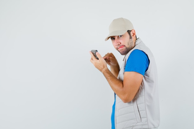 Jeune homme à l'aide de la calculatrice, qui sort la langue en t-shirt, veste et à la pensif.