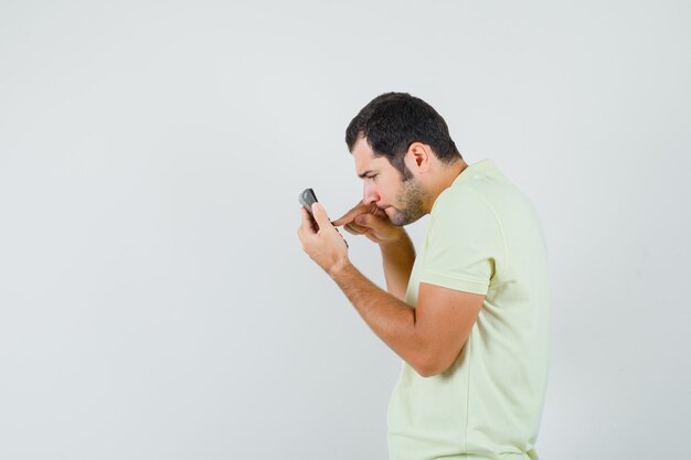 Jeune homme à l'aide de la calculatrice en t-shirt et à la recherche de sérieux.