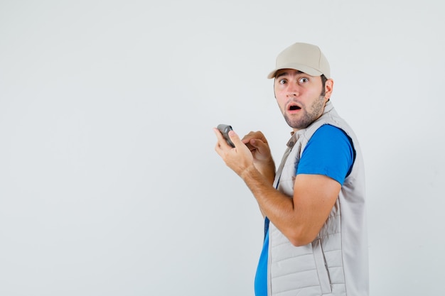 Jeune homme à l'aide de la calculatrice en t-shirt, veste et à la perplexité. .