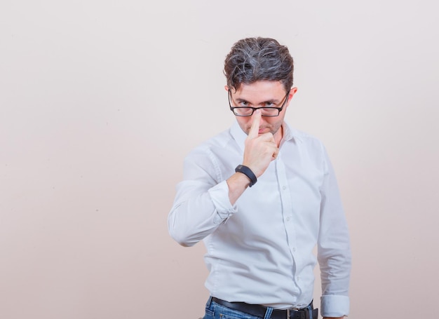 Jeune homme ajustant ses lunettes en chemise blanche, jeans et semblant sérieux