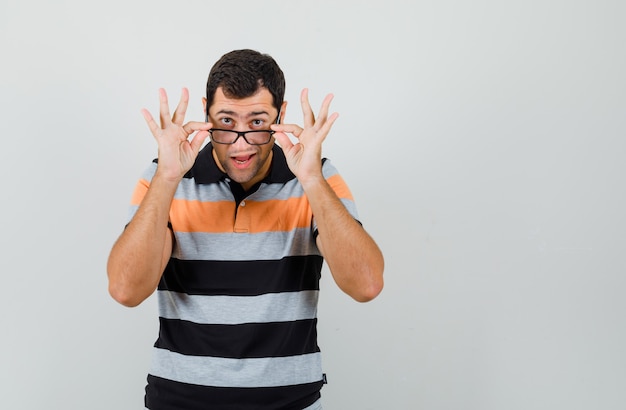 Jeune homme ajustant ses lunettes en t-shirt, lunettes et à la confiance. espace pour le texte
