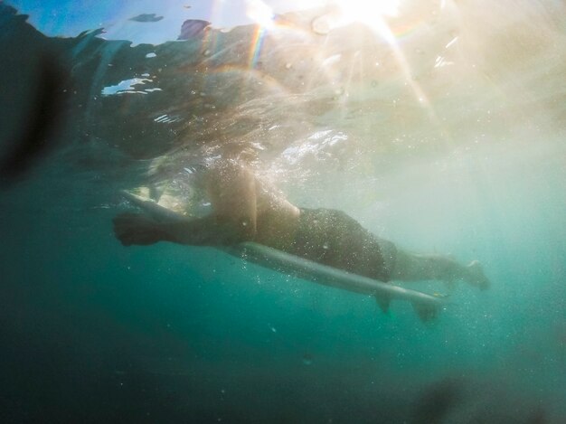 Jeune homme allongé sur une planche de surf dans l&#39;eau bleue