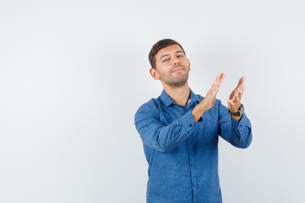 Jeune homme applaudissant après une excellente présentation en chemise bleue et l'air gai. vue de face.