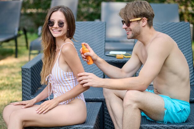 Jeune homme appliquant de la crème spf sur son corps de femme