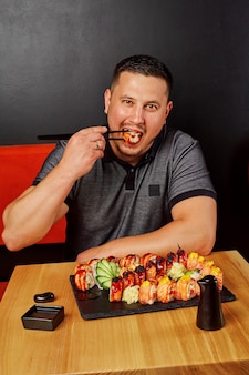 Jeune homme appréciant de manger des sushis à table dans un restaurant japonais