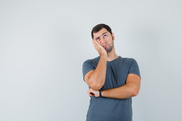 Jeune homme appuyé contre la joue sur la paume surélevée en t-shirt gris et à la pensif