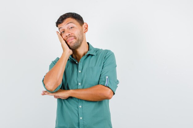 Jeune homme appuyé sur la joue sur la paume surélevée en chemise et à la joyeuse