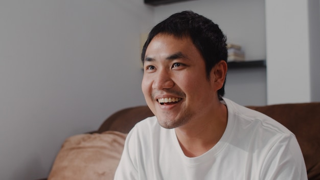 Jeune homme asiatique à l'aide de manette de jeu jouer à des jeux vidéo à la télévision dans le salon, un homme se sentant heureux à l'aide d'une journée de détente allongé sur un canapé à la maison. Les hommes jouent à des jeux se détendre à la maison.