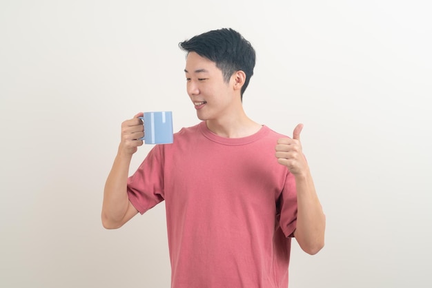 Jeune homme asiatique tenant une tasse de café avec un visage souriant sur fond blanc