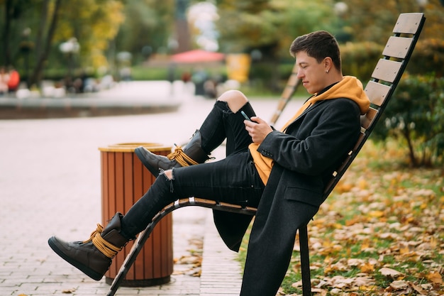 Jeune homme assis sur un banc dans le parc et écouter de la musique