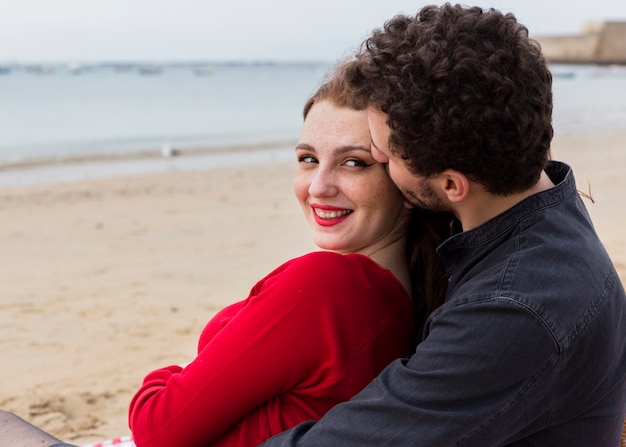 Jeune homme assis sur le bord de mer sablonneux et embrassant une femme