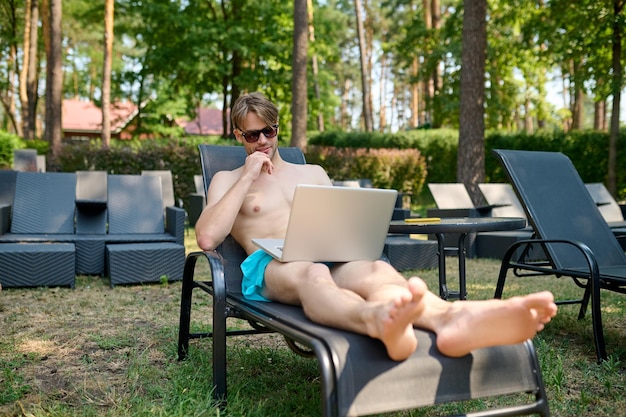 Un jeune homme assis sur une chaise longue avec un ordinateur portable