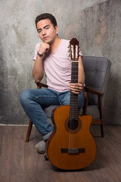 Jeune homme assis sur une chaise et tenant la guitare. Photo de haute qualité