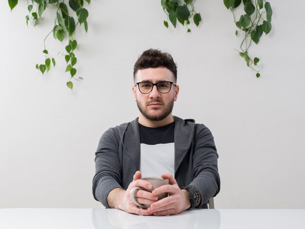 jeune homme assis dans des lunettes montres veste grise avec plante sur blanc