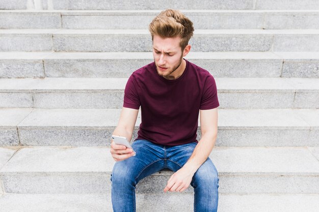 Jeune homme assis sur l&#39;escalier tenant le téléphone mobile