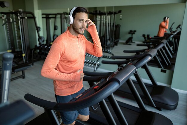 Jeune homme athlétique faisant du jogging sur une piste de course tout en faisant de l'exercice dans un club de santé