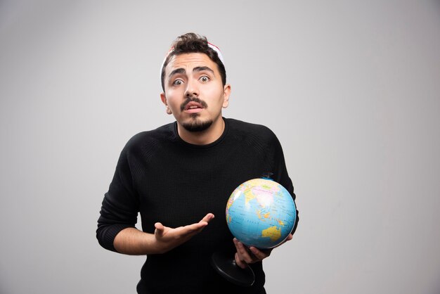 Jeune homme au chapeau du père Noël montrant un globe.