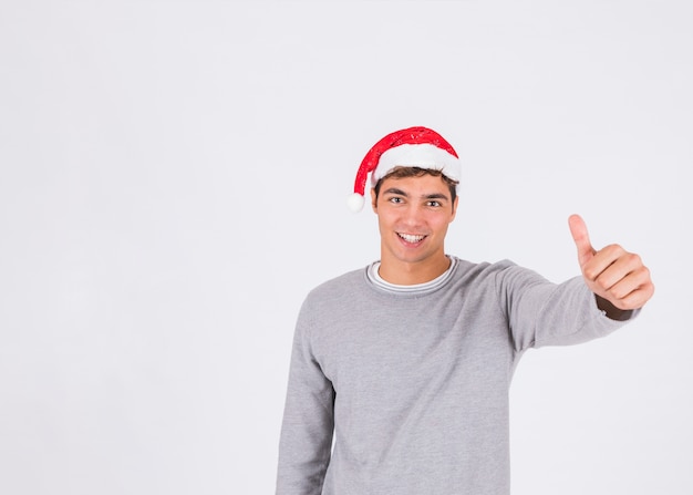 Jeune homme au chapeau de Noël avec le pouce vers le haut