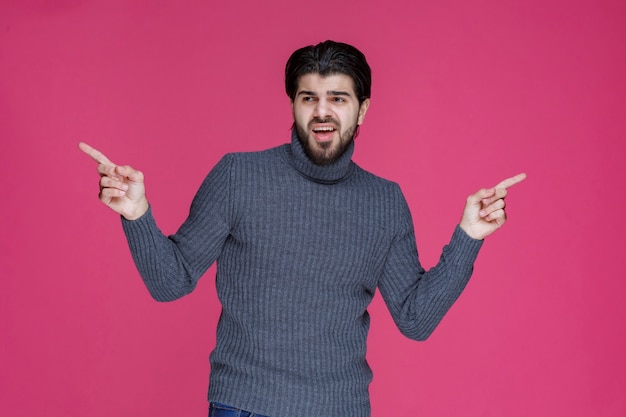 Jeune homme aux cheveux longs et à la barbe montrant ou pointant quelque chose avec ses doigts.