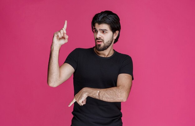 Jeune homme aux cheveux longs et à la barbe montrant ou pointant quelque chose avec ses doigts.