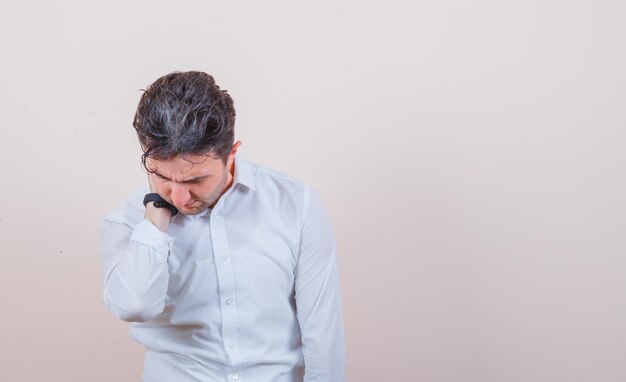 Jeune homme ayant des douleurs au cou en chemise blanche et à l'aise