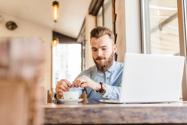 Photo gratuite jeune homme ayant une tasse de café avec ordinateur portable sur le bureau