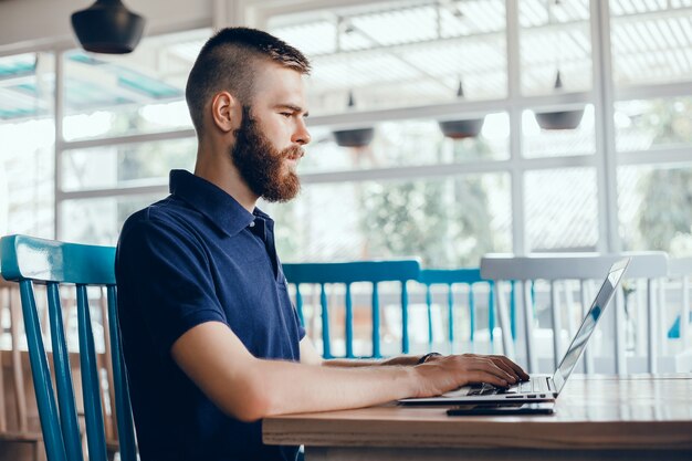 jeune homme avec une barbe travaille dans un café, pigiste utilise un ordinateur portable, fait un projet