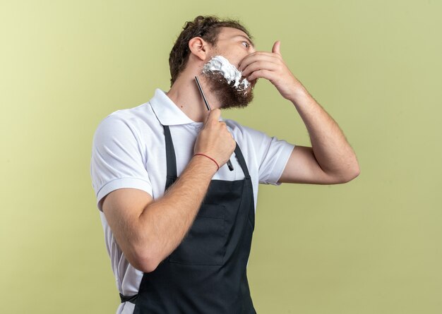 Jeune Homme Barbier Portant La Barbe De Rasage Uniforme Avec Un Rasoir Droit Isolé Sur Fond Vert Olive