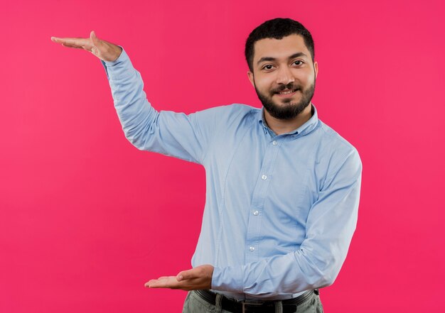Jeune homme barbu en chemise bleue montrant un geste de grande taille avec les mains, symbole de mesure