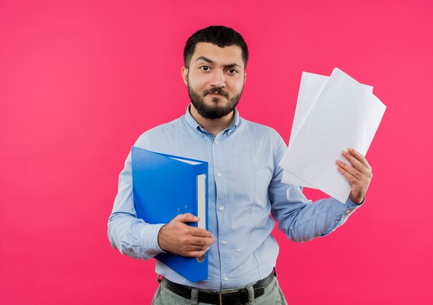 Jeune homme barbu en chemise bleue tenant le dossier et les pages blanches mécontent